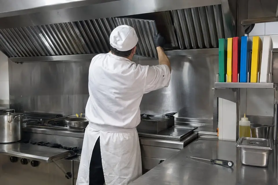 Trabajador de espaldas con ropa blanca de cocina retirando los filtros de la campana de una cocina de restaurante