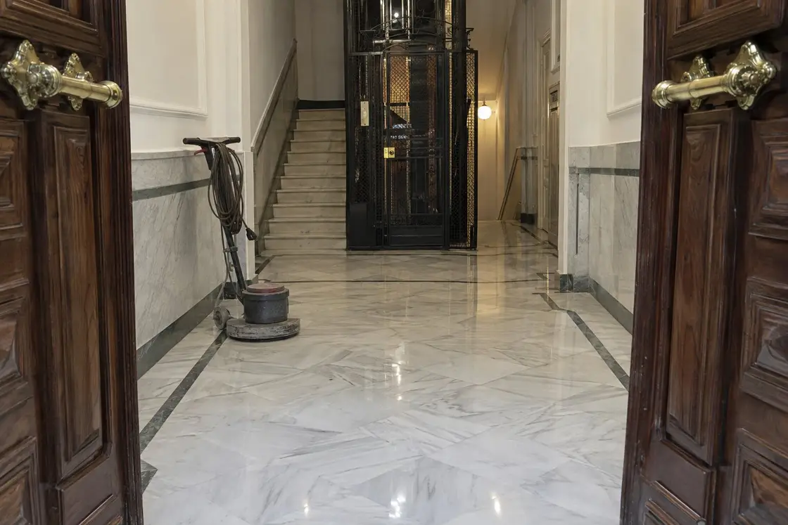 Portal de una finca antigua con el suelo de mármol blanco recién cristalizado y una rotativa junto a la pared