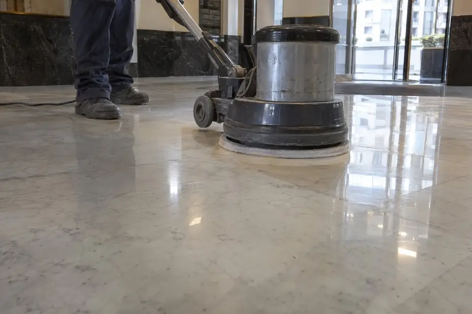 Máquina rotativa cristalizando un suelo de mármol blanco en un vestíbulo de oficinas; solo se ven las piernas del operario